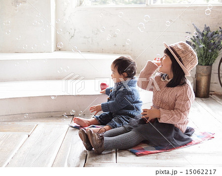 白い部屋の中で座ってシャボン玉と遊んでいる赤ちゃんと女の子の写真素材