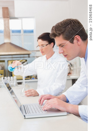 Scientist working attentively with laptop and another with beake Scientist working attentively with laptop and another with beake 15068468