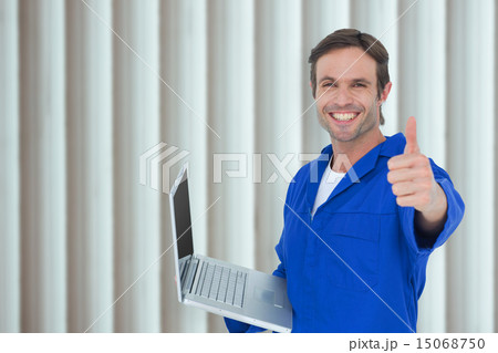 Composite image of mechanic holding laptop while showing thumbs 15068750