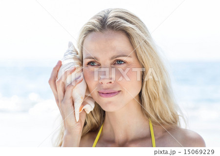Smiling pretty blonde listening the seashell 15069229