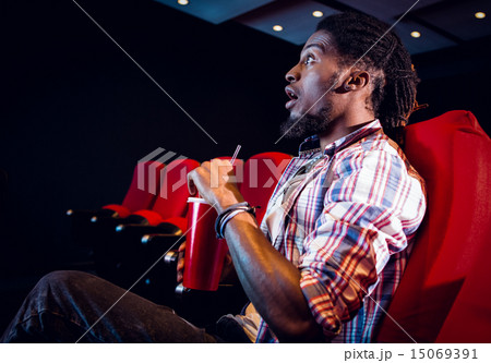 Young man watching a film and drinking soda Young man watching a film and drinking soda 15069391
