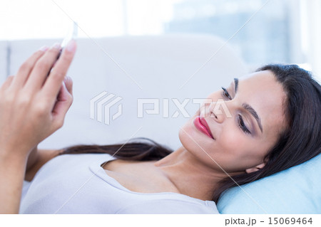 Smiling beautiful brunette relaxing on the couch and using her p 15069464