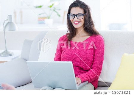 Smiling beautiful brunette using her laptop on the couch Smiling beautiful brunette using her laptop on the couch 15073821