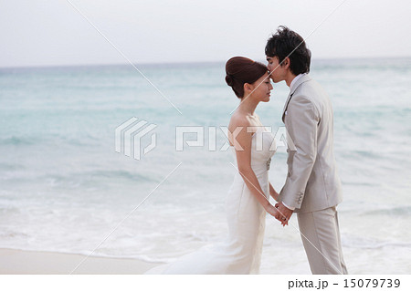 海をバックにビーチウェディング おでこにキス新郎新婦横の写真素材