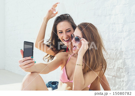 Female friends laughing having fun taking selfie together wearing bikini bra swimsuit summer sunny d Female friends laughing having fun taking selfie together wearing bikini bra swimsuit summer sunny d 15080782
