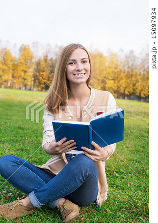 Student sitting on green grass with opened book Student sitting on green grass with opened book 15097934