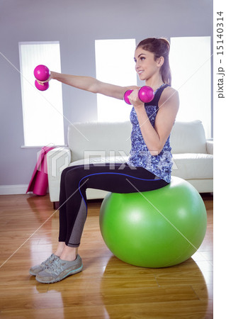 Fit woman lifting dumbbells on exercise ball 15140314