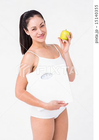 Smiling brunette holding weighing scales and apple Smiling brunette holding weighing scales and apple 15140355