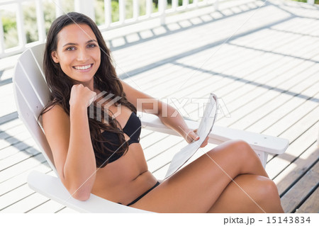 Pretty brunette sitting on a chair and reading magazine Pretty brunette sitting on a chair and reading magazine 15143834