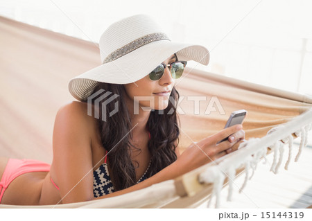 Pretty brunette relaxing on a hammock and texting with her mobil Pretty brunette relaxing on a hammock and texting with her mobil 15144319