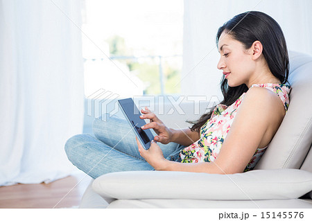 Pretty brunette using tablet on couch Pretty brunette using tablet on couch 15145576