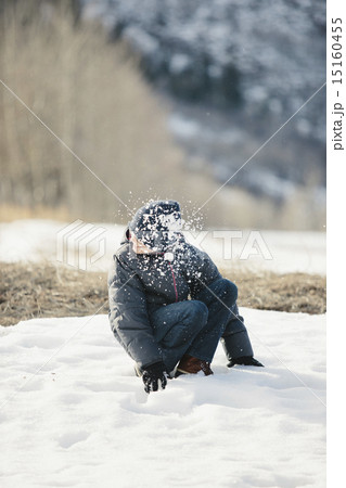 A boy in a blue coat and woolly hat turning his head from a snowball which has hit him. 15160455
