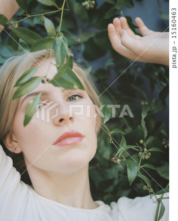 A blond haired woman looking wistfully through a vine with green leaves. 15160463