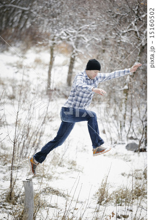 A man leaping from one post to another in the snowy woodland. 15160502
