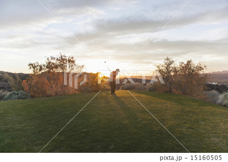 A man taking a shot off a golf tee on a golf course into the sunset.  15160505