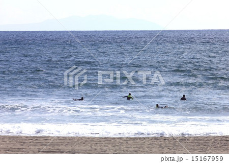 遠方に伊豆大島を望み 人気ない冬の湘南の海でサーフィンを楽しむサーファー達の写真素材