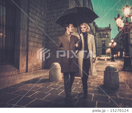 Elegant couple with umbrella walking outdoors  15270124