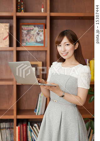 ノートパソコンを見る本棚の前の女性 15307444