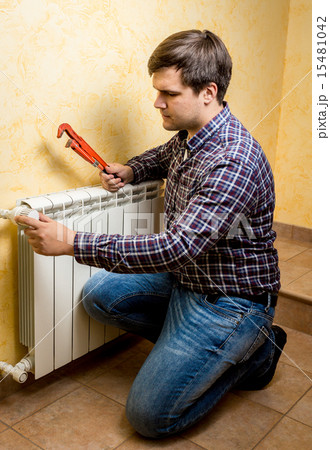 handyman fixing heating radiator with red plumber pliers 15481042