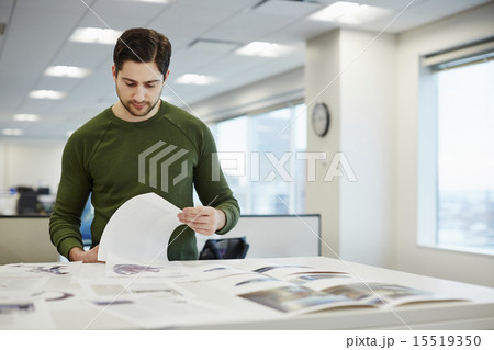 A man in an office checking proofs of printed pages. A man in an office checking proofs of printed pages. 15519350