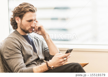 A bearded man sitting frowning and checking his phone. 15519379