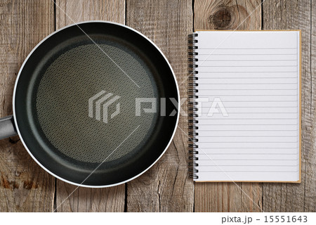 Frying pan and recipe book on wooden background 15551643