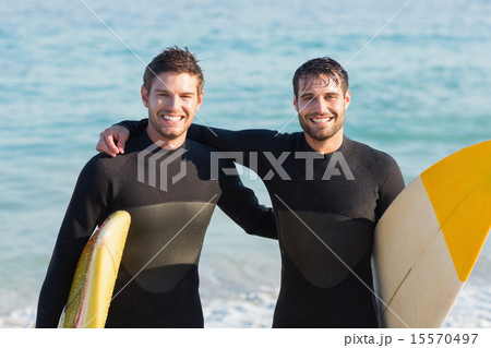 Two men in wetsuits with a surfboard on a sunny day Two men in wetsuits with a surfboard on a sunny day 15570497