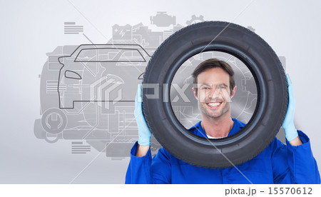 Composite image of confident mechanic looking through tire 15570612