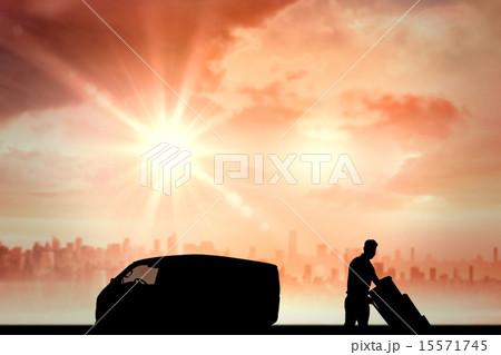 Composite image of happy delivery man pushing trolley of boxes 15571745