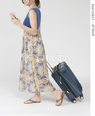 キャリーバッグを引きながらスマホを見る女性の写真素材