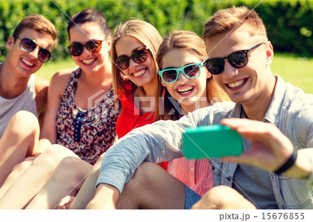 smiling friends with smartphone sitting on grass 15676855