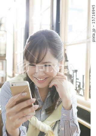 カフェで携帯電話を見る笑顔の女性 15716945