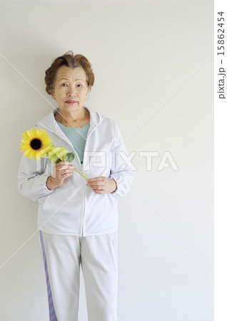 白い部屋でひまわりの花を持っている元気な高齢者女性 15862454
