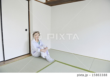 何もない部屋で一人で三角座りをしている孤独な高齢者女性の写真素材