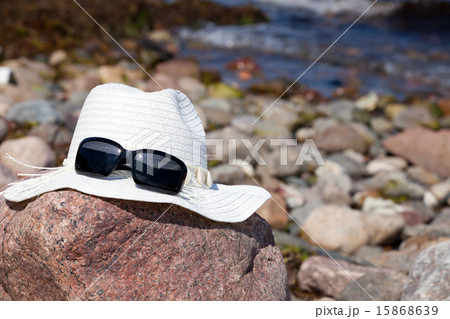 White straw hat with sunglasses lies on a big rock White straw hat with sunglasses lies on a big rock 15868639