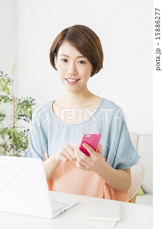 パソコンの前でスマホを操作する若い女性 15886277