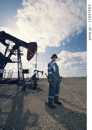 A man in overalls and hard hat at a pump jack in open ground at an oil extraction site. 15897664