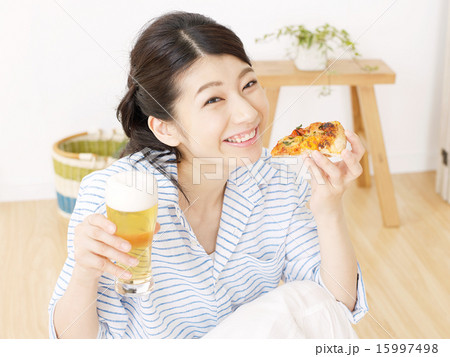 部屋でビールとピザを食べる女性の写真素材