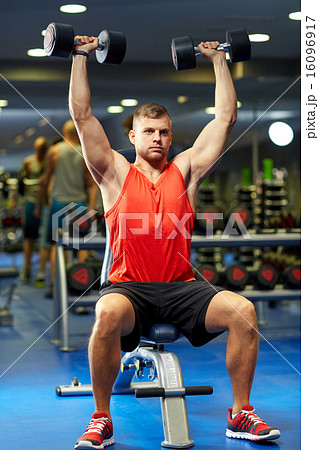 young man with dumbbells flexing muscles in gym 16096917