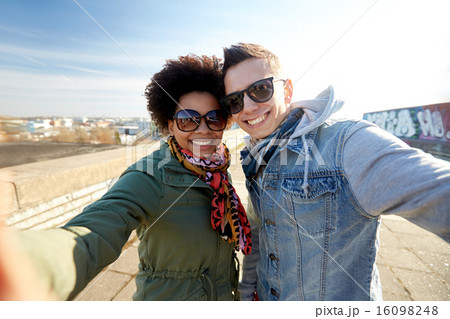 happy teenage couple taking selfie on city street 16098248