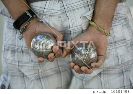 A boules player with one metal ball in each hand, held behind his back.  16101493