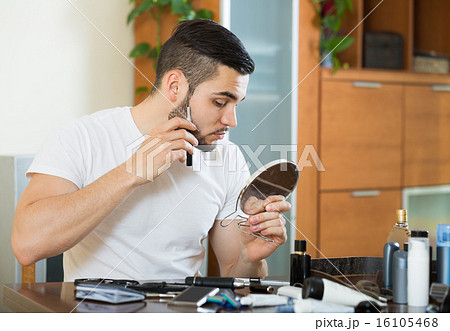 guy looking at mirror and shaving beard with trimmer 16105468