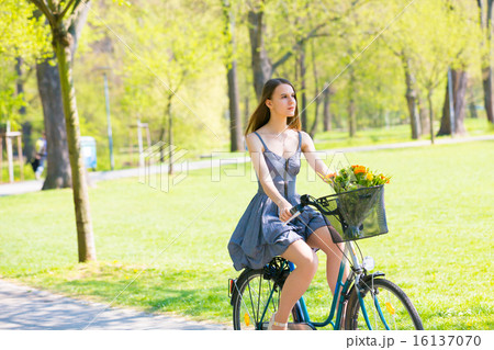 Young woman in short grey dress with long hair rides a bicycle w Young woman in short grey dress with long hair rides a bicycle w 16137070