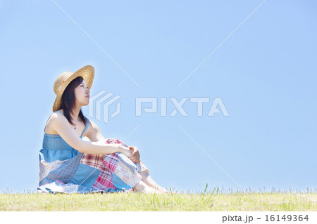 青空の下で丘に座りくつろぐ女性 16149364