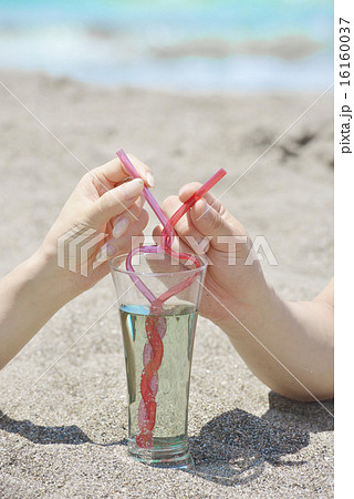 ビーチで寄り添いハート型のストローでドリンクを飲むカップルの手の写真素材