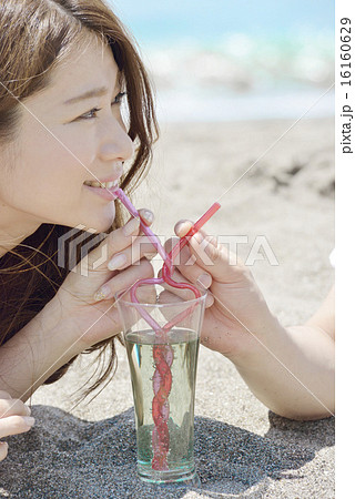 ビーチで寄り添いハート型のストローでドリンクを飲むカップルの写真素材