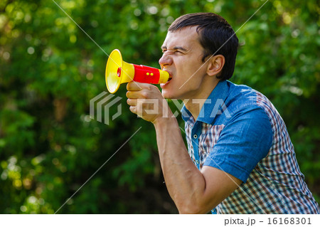 The man in the street holding a plastic speaker shouts on green The man in the street holding a plastic speaker shouts on green 16168301