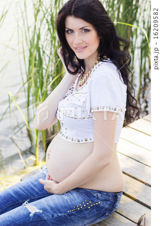 Pregnant brunette girl sitting on bridge near river Pregnant brunette girl sitting on bridge near river 16209582