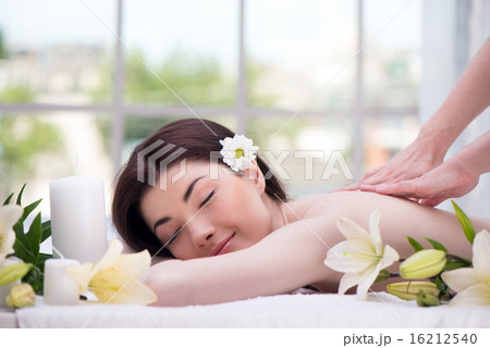 Relaxed woman with flowers in spa center enjoying massage Relaxed woman with flowers in spa center enjoying massage 16212540
