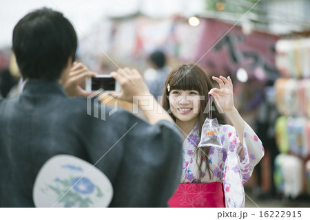 お祭りで金魚の入った袋を持ち写真を撮るカップルの写真素材